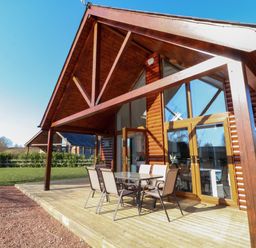 A wooden cabin with glass doors and an outdoor dining table with chairs on a deck at The Green Monkey in North Hykeham