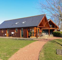 A wooden house with a patio and outdoor furniture on a grass lawn with a gravel path at The Green Monkey in North Hykeham
