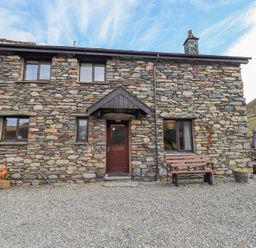 Stone cottage exterior with wooden door windows bench and outdoor seating at Low Wood View in Hartsop