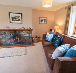 A living room with a stone fireplace a brown sofa with blue cushions and a window with curtains at Low Wood View in Hartsop
