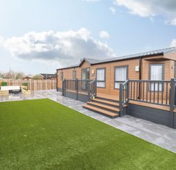 A patio area with artificial grass and wooden mobile homes at Blossom Vale Lodge in Evesham