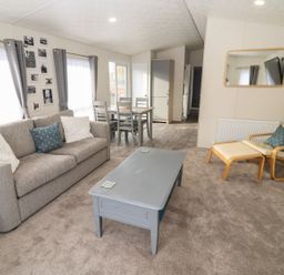 A living room with a sofa, armchair, coffee table, dining table, and chairs at Blossom Vale Lodge in Evesham
