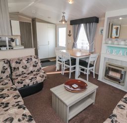 A living room with a floral sofa, wooden coffee table, dining table with chairs, and a fireplace at Rose Bank D8 in Primrose Valley