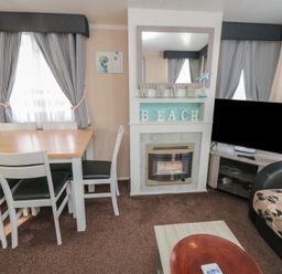 A dining table with chairs next to a fireplace with decorative beach letters and a television in a living room at Rose Bank D8 in Primrose Valley