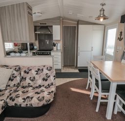 A combined kitchen and dining area with a floral patterned sofa a wooden dining table with chairs and kitchen appliances at Rose Bank D8 in Primrose Valley