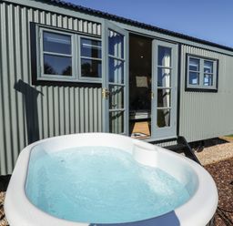 An outdoor hot tub in front of a corrugated metal cabin with open double doors at Buttercup in Ashby-cum-Fenby near Waltham