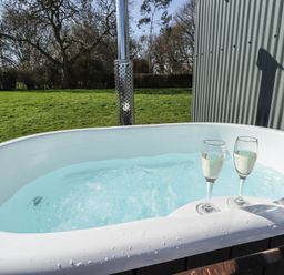 An outdoor hot tub with two glasses of champagne and a grassy field in the background at Buttercup in Ashby-cum-Fenby near Waltham