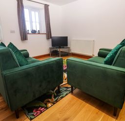 A room with two green sofas facing a small TV on a corner table at The Baler House in Hayle