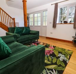 A living room with green sofas floral rug wooden staircase and a television at The Baler House in Hayle