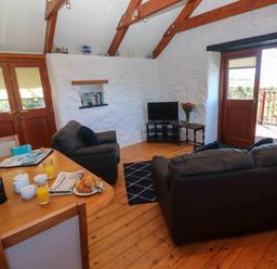 A living room with leather sofas a TV on a stand and a table with breakfast items at Bay View Barn in Hayle