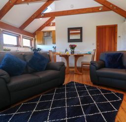 A living room with two sofas a dining table and chairs a kitchen area with wooden beams on the ceiling at Bay View Barn in Hayle