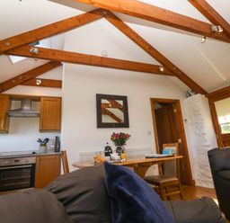 A kitchen and dining area with wooden beams on the ceiling and a table with flowers and croissants at Bay View Barn in Hayle