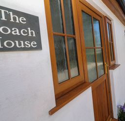 An exterior wall with a wooden door and window next to a sign that says The Coach House at The Coach House in Hayle