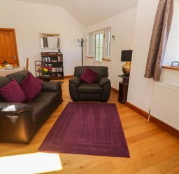A living room with black leather sofa and armchair with purple cushions and rug at The Coach House in Hayle