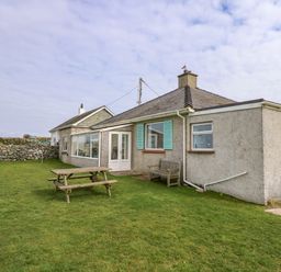 A house with a wooden picnic table and bench on a lawn at Tegawelon in Llandanwg near Harlech