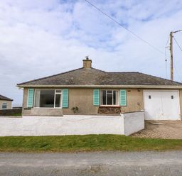 A single-story house with two windows and a garage door and a low white wall in front at Tegawelon in Llandanwg near Harlech