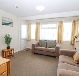 A living room with two sofas a small wooden table with a plant and a door with windows at Chalet 21 in Newport Norfolk