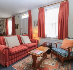 A sitting room with a red striped sofa, a wooden armchair with blue striped cushions, a wooden coffee table, and red curtains at The Townhouse in Salisbury