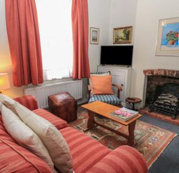 A living room with a striped red sofa cushions a wooden coffee table an armchair a small TV and a brick fireplace at The Townhouse in Salisbury