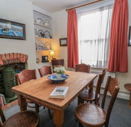 A dining room with wooden table and six chairs a fireplace with brick surround shelves with plates and a window with red curtains at The Townhouse in Salisbury