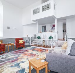 A living room with two red armchairs a gray sofa a wooden side table a colorful rug and white decorative balcony at Trelowth Chapel in Polgooth