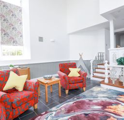 A sitting area with two patterned armchairs and a small wooden table in a room with white walls and tiled floor at Trelowth Chapel in Polgooth