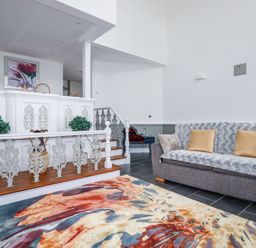 A living room with a gray sofa and a multicolored rug near stairs with decorative railing at Trelowth Chapel in Polgooth