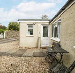 A patio area with a table and two chairs outside a cream-colored house at Spring Cottage in Birdlip near Brockworth