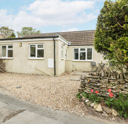 A single-story house with a gravel driveway a stone wall with flower bed and outdoor table and chairs at Spring Cottage in Birdlip near Brockworth
