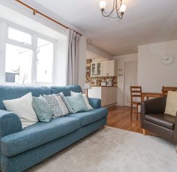 A living room with a blue sofa and pillows a brown armchair a dining table with chairs and a kitchen area at Spring Cottage in Birdlip near Brockworth