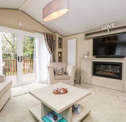 A living room with beige chairs a wooden coffee table a fireplace and a mounted TV at Water's Reach White Cross Bay Holiday Park near Troutbeck Bridge
