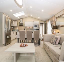An open plan living room and kitchen with a sofa coffee table dining table and chairs at Water's Reach White Cross Bay Holiday Park near Troutbeck Bridge