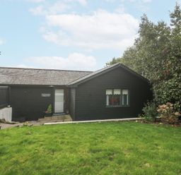 A black wooden house with a tiled roof and a green lawn in front with bushes on one side at Chy Benyngoth in Hayle