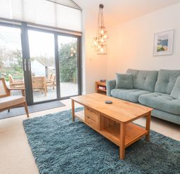 A living room with a green sofa a wooden coffee table a blue rug and large sliding glass doors at Chy Benyngoth in Hayle