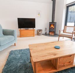 A living room with a blue armchair wooden coffee table and a chair near a wood stove and a TV at Chy Benyngoth in Hayle