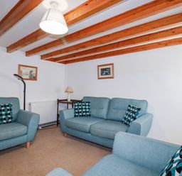 A sitting room with blue armchairs and a sofa with patterned cushions under wooden ceiling beams at Pennine in Veryan