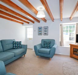 A living room with blue sofas and a wooden TV stand under exposed wooden ceiling beams at Pennine in Veryan