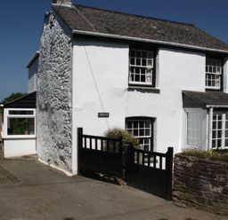 A white stone house with black-trimmed windows and a black gate in front at Pennine in Veryan