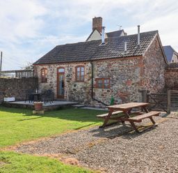 An outdoor area with a stone cottage patio table and chairs a wooden picnic table and a grass lawn at The Yarde Annexe Pen Elm near Taunton