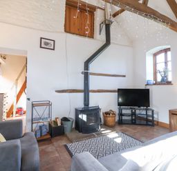 A living room with a wood burning stove television armchairs and wooden ceiling beams at The Yarde Annexe in Pen Elm near Taunton