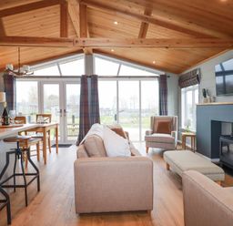 A living room with sofas armchair ottoman wood stove and large windows at 6 Meadow Retreat in Dobwalls