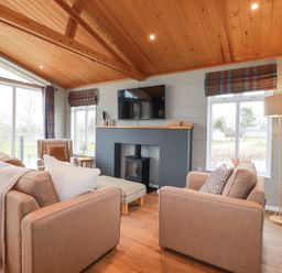 A living room with beige sofas a wood stove television and a wooden ceiling at 6 Meadow Retreat in Dobwalls