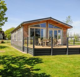 A wooden cabin with a glass enclosed deck and outdoor furniture on a grassy lawn at 17 Meadow Retreat in Dobwalls