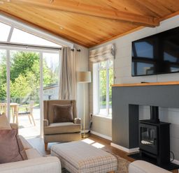 A living room with a sofa armchair ottoman wood stove and television at 17 Meadow Retreat in Dobwalls
