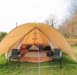 A bell tent with two black chairs outside a bed inside on grass at Bell tent 3 Camerton near Timsbury