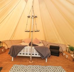 Interior of a bell tent with a bed a candle holder wooden crates and decorative items at Bell tent 3 Camerton near Timsbury