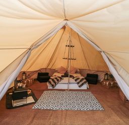 A bell tent interior with a bed cushions a stove and a patterned rug at Bell tent 4 in Camerton near Timsbury