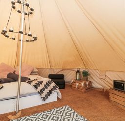 A tent interior with a bed blankets crates and a patterned rug at Bell tent 4 in Camerton near Timsbury