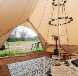 The interior of a bell tent with a bed, rugs, a wood stove, and two chairs outside at Bell tent 4 in Camerton near Timsbury