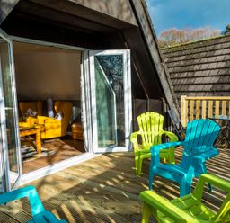 A wooden deck with green and blue plastic chairs outside a room with yellow armchairs at Valley Lodge 40 in St Ann's Chapel Cornwall